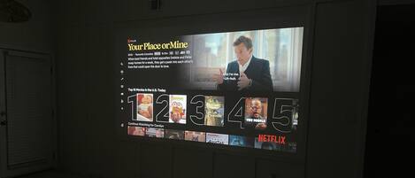 Una pantalla de proyector mostrando la película 'Your Place or Mine' con una lista de las películas más populares en la plataforma Netflix.