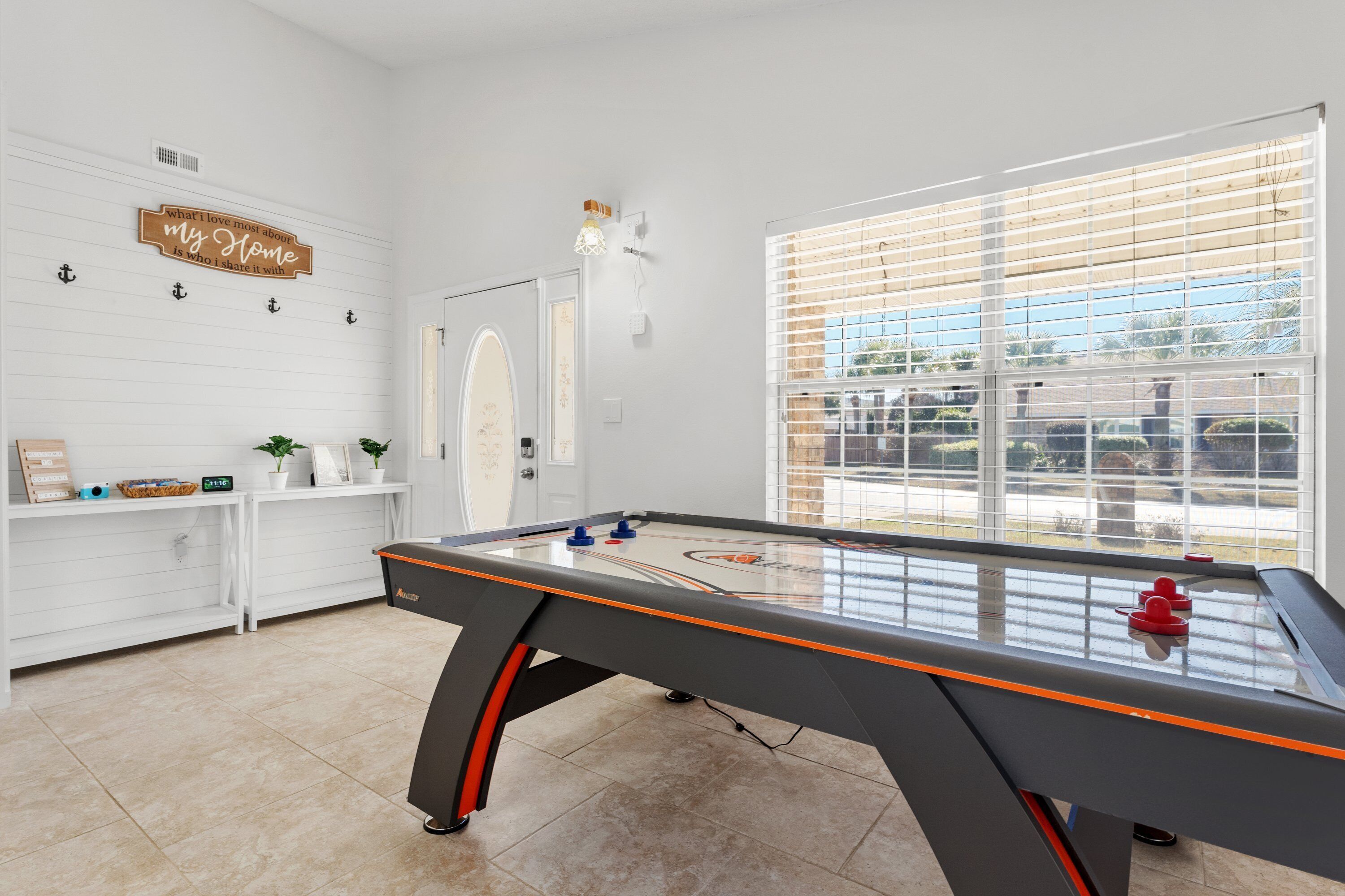 Uma mesa de bilhar em um ambiente com paredes brancas, uma janela com persianas e uma placa na parede.