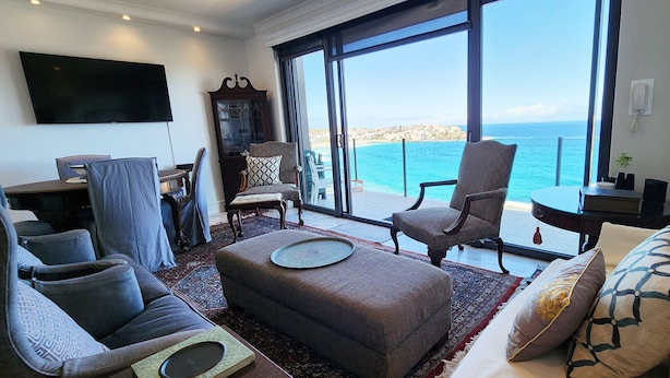 Un vaste salon doté d’une grande fenêtre donnant sur la mer, d’un téléviseur à écran plat fixé au mur et d’un coin salon confortable avec un canapé et des fauteuils.