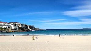 Une plage bordée de bâtiments sur les côtés gauche et droit, un ciel dégagé et une mer calme.