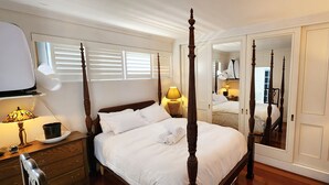 Un lit à baldaquin avec du linge de lit blanc, une lampe de chevet et un miroir qui reflète la pièce.