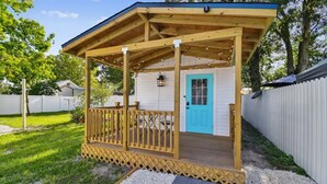 Une terrasse en bois avec une porte bleue, entourée d’une clôture blanche, et un espace couvert agrémenté de guirlandes lumineuses.