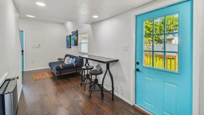 Un espace de vie compact avec une porte de couleur turquoise, un canapé, une petite table et une fenêtre donnant sur un paysage verdoyant.