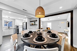 A modern kitchen with white cabinets, a dining table set with black bowls, and a wicker pendant light.