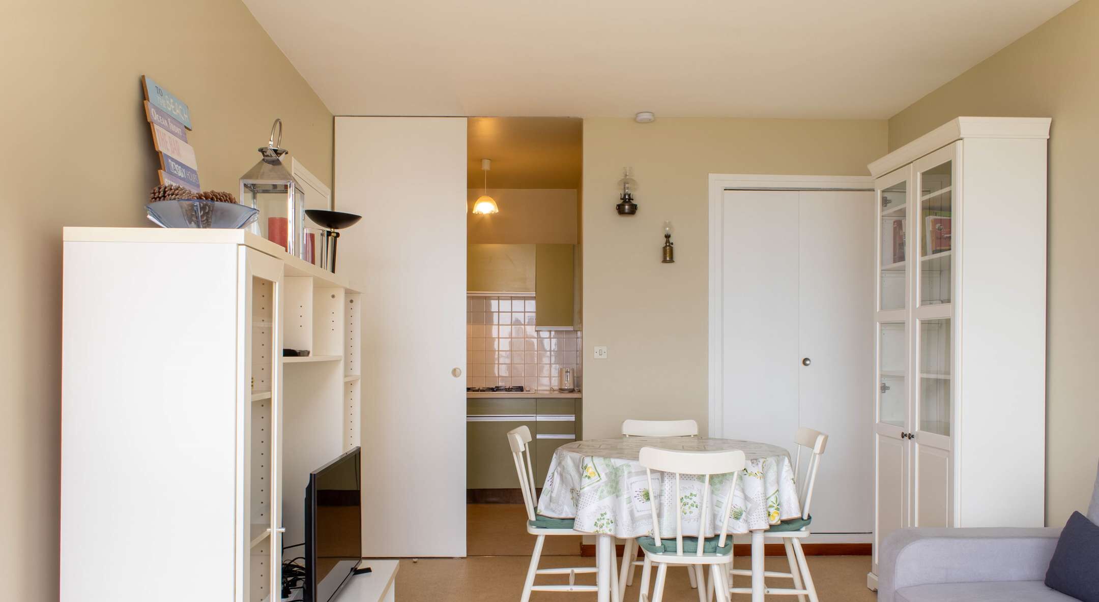 Un espacio habitable compacto con zona de comedor, kitchenette y un armario blanco.