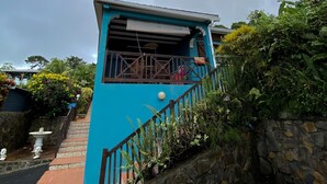 Ein blaues Gebäude mit Balkon, umgeben von üppigem Grün und einer Steinmauer.