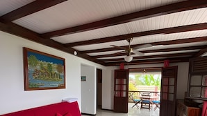 Ein geräumiges Zimmer mit einem roten Sofa, einem Holztisch und einem Deckenventilator.