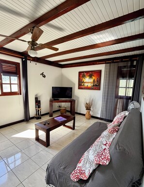 Ein Wohnzimmer mit einer Couch, einem Couchtisch, einem Fernseher und einem Deckenventilator.
