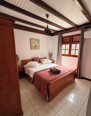 A bedroom with a wooden bed, a nightstand, a ceiling fan, a window with curtains, and a wall-mounted artwork.