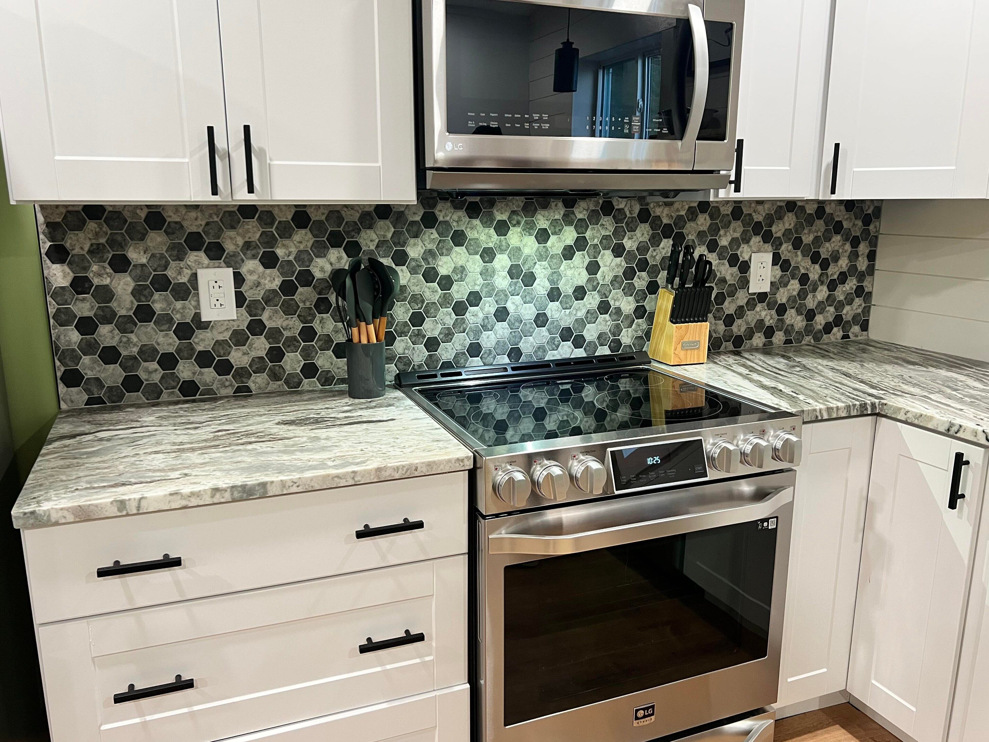 A modern kitchen with white cabinets, a stainless steel stove, and a microwave.
