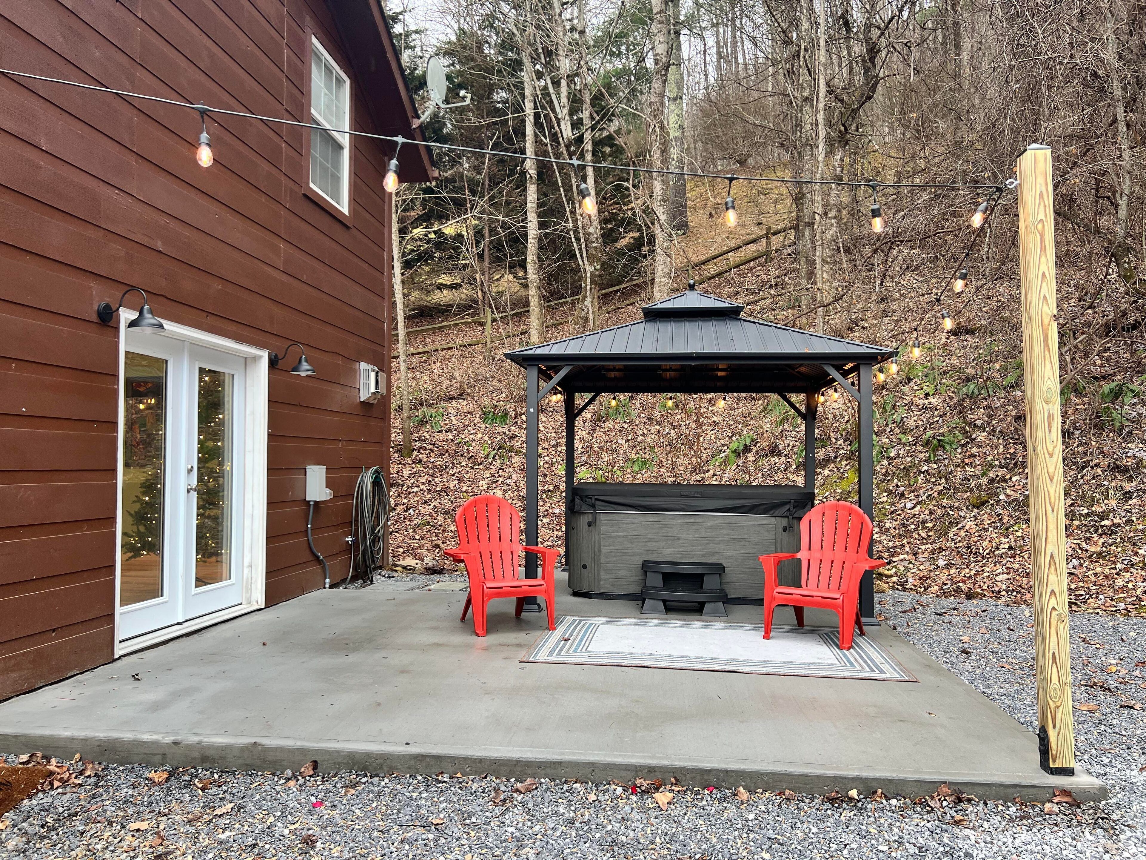 A wooden house with a covered patio area featuring two red chairs and a small fire pit.