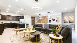 A modern living room with a sofa, two round tables, and a kitchen area with dark cabinets and a white refrigerator. - 10BR Villa w/ Pool, Theater Loft & Cabanas (Davenport)