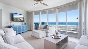 A modern living room with a large window, a ceiling fan, and a view of the beach.