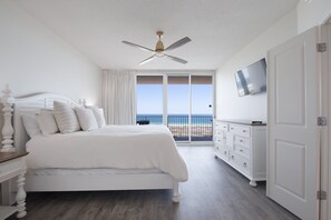 Un dormitorio con cama, ventilador de techo, televisión, cómoda y vista al mar.