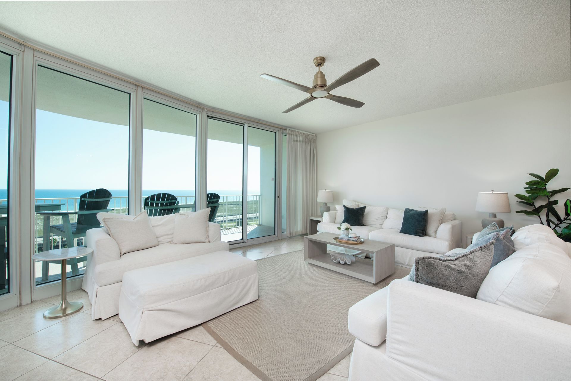 A spacious living room with a large window, a ceiling fan, and a view of the ocean.