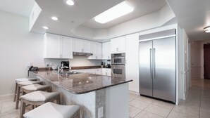 A modern kitchen with white cabinets, a stainless steel refrigerator, a granite countertop, and a built-in island with bar stools.