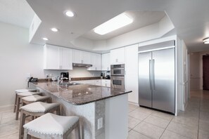 Una cocina moderna con armarios blancos, un refrigerador de acero inoxidable, una encimera de granito y una isla integrada con taburetes de bar.