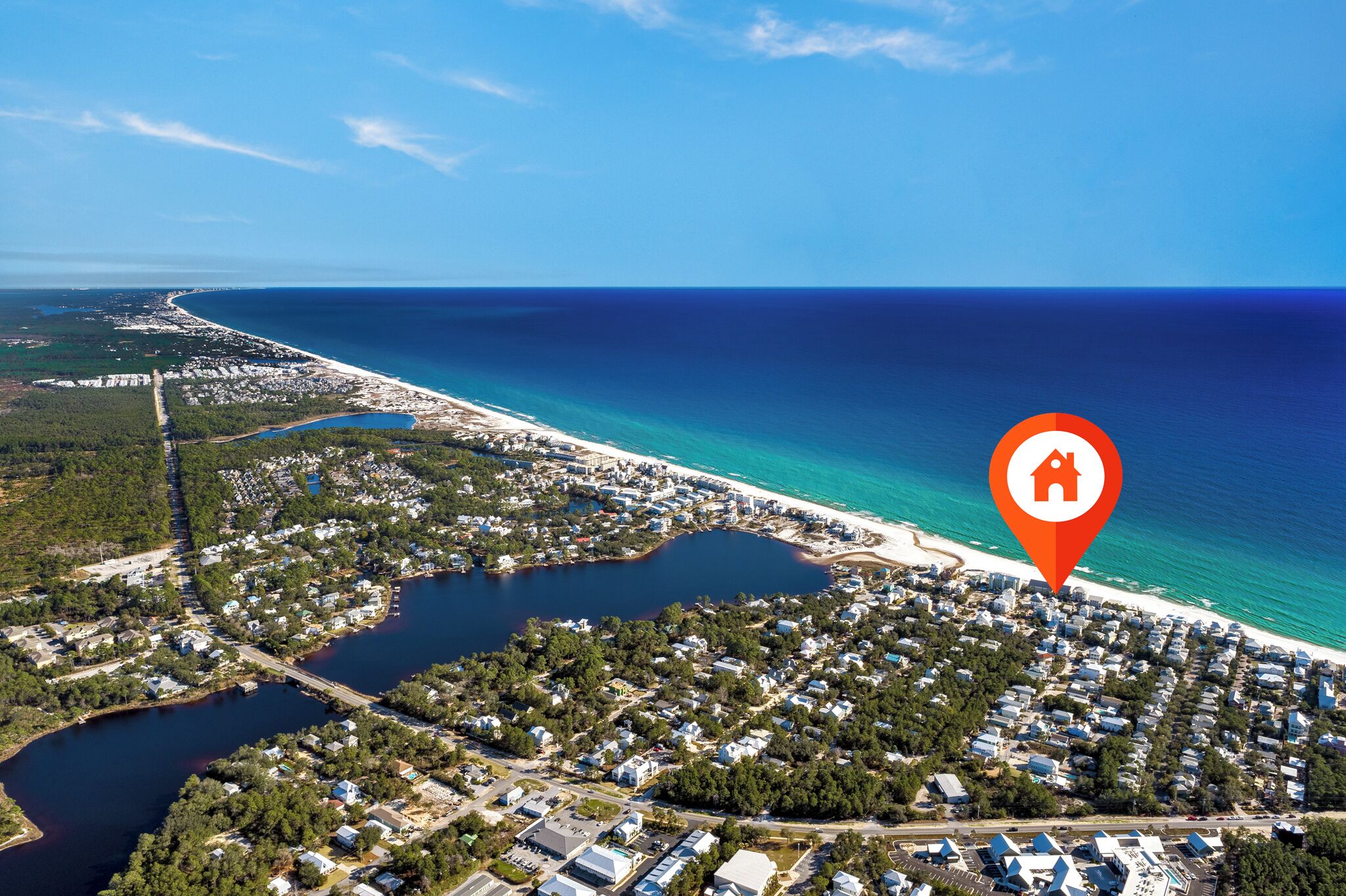 An aerial view of a coastal town with a beach, a marina, and a dense residential area.