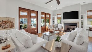 A modern living room with white furniture, a ceiling fan, a fireplace, and large windows. - Ocean View ☀️1 Lot from the Gulf | 52 10-Star Reviews | Beach Gear ☀️Comm Pool (Santa Rosa Beach)