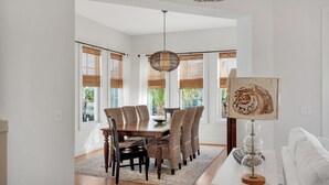 A dining area with a wooden table, wicker chairs, and a hanging light fixture. - Ocean View ☀️1 Lot from the Gulf | 52 10-Star Reviews | Beach Gear ☀️Comm Pool (Santa Rosa Beach)