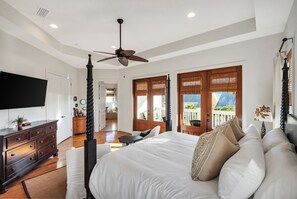 Une chambre dotée d’un grand lit, d’un ventilateur de plafond, d’une télévision et de portes en bois donnant sur un balcon.