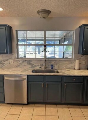 Enjoy a kitchen with a large window offering a view of the outdoors, featuring dark cabinetry and stainless steel appliances.