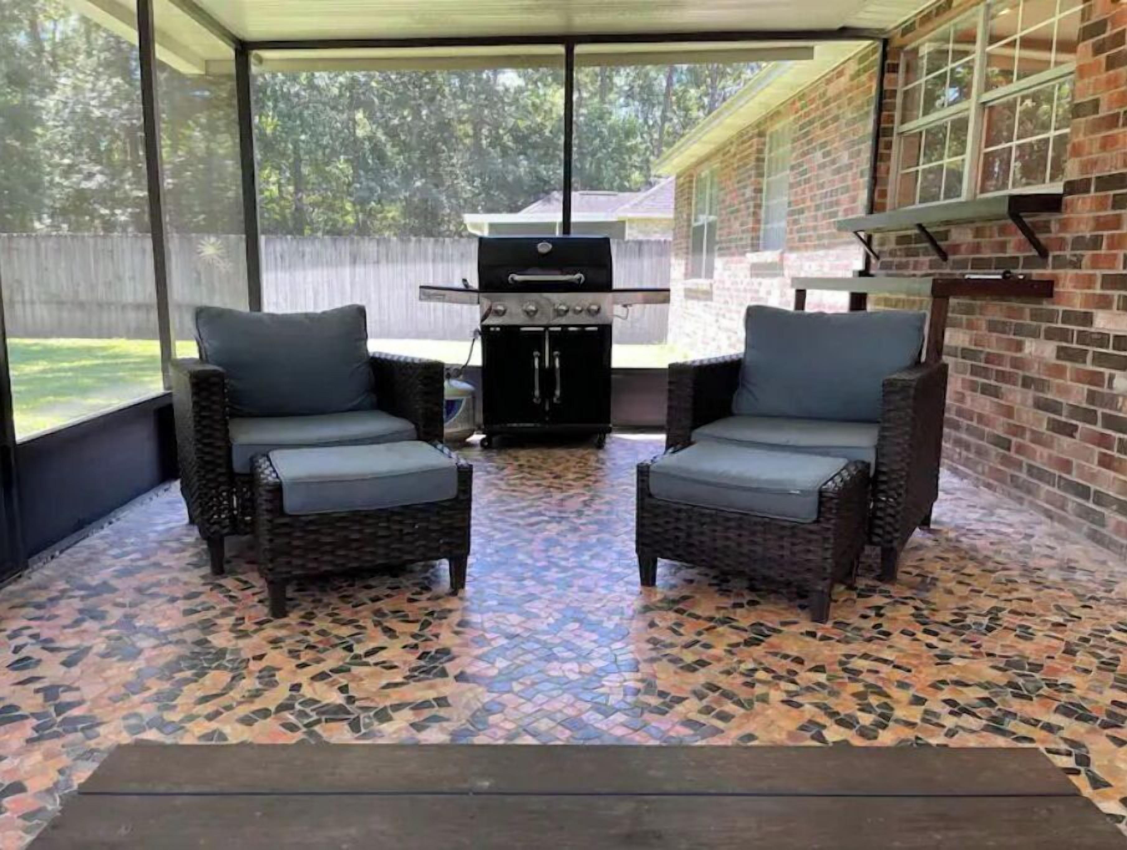 A covered patio area with two wicker chairs, a grill, and a patterned tile floor.