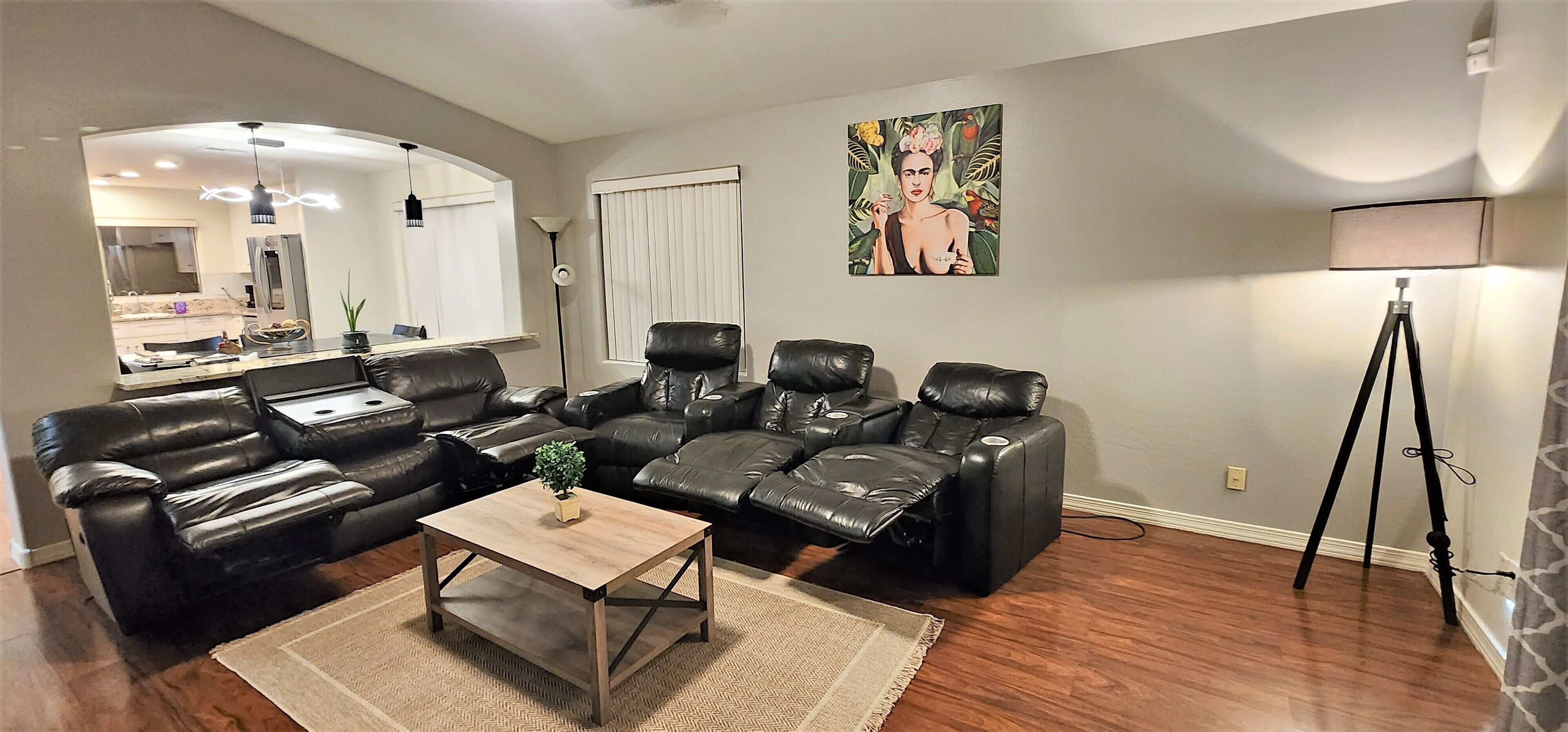 A living room with a black leather sofa set, a wooden coffee table, and a painting on the wall.