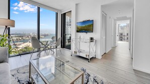 Un soggiorno moderno con un tavolo in vetro, sedie, una TV e vista sulla città.