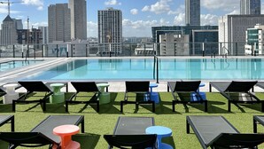 Una piscina sul tetto con lettini e uno skyline cittadino sullo sfondo.
