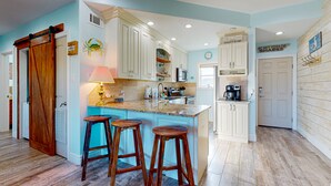 Una cocina con una isla central, taburetes de bar, una estación de café y una puerta con un letrero.