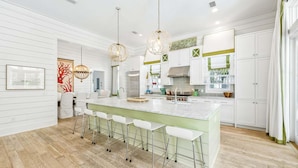 A modern kitchen with a central island, bar stools, pendant lighting, and white cabinetry. - Private Pool + 6 Seat Golf Cart that is Close to SandHill Pool - WaterColor | Lake District Home (Santa Rosa Beach)