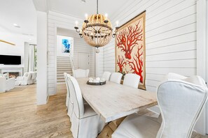 Un comedor con una mesa de madera, sillas blancas, una araña de cristal y un cuadro abstracto de gran tamaño en la pared.