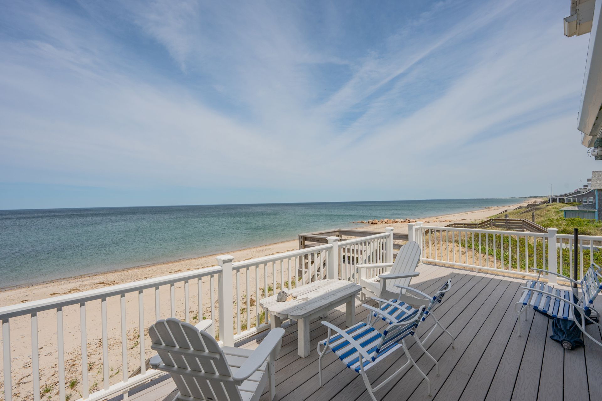 A wooden deck with white railings, blue and white striped lounge chairs, and a small table with a chair.