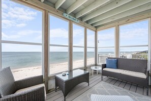 Ein überdachter Sitzbereich im Freien mit Rattanmöbeln, einem Glastisch und Blick auf den Strand.