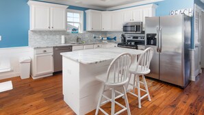 A kitchen with white cabinets, a stainless steel refrigerator, and a marble countertop.