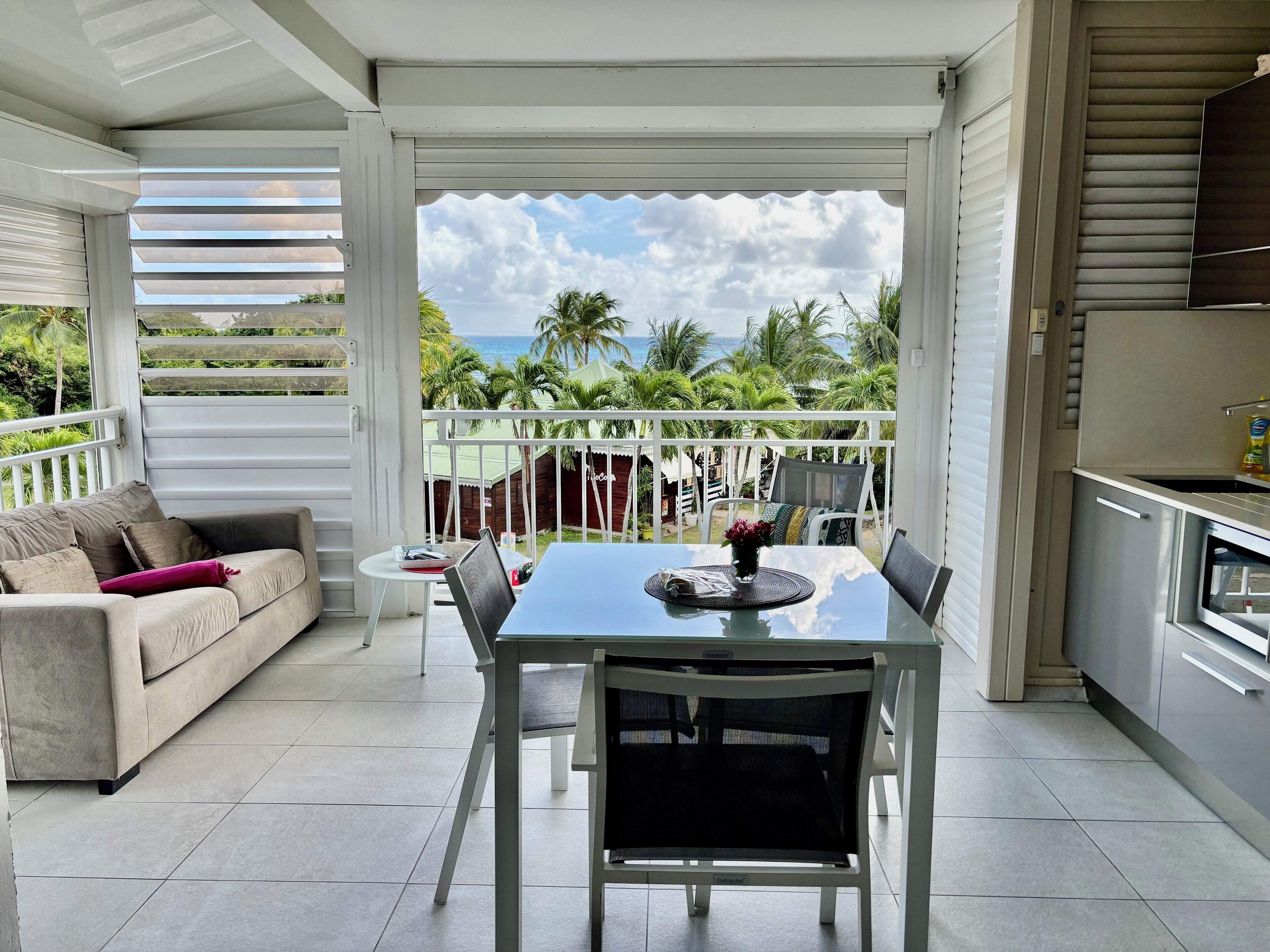 A balcony with a dining table and chairs, a sofa, and a kitchen area.