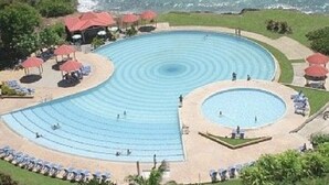 Une grande piscine circulaire, avec plusieurs niveaux de marches menant à l’eau, entourée de chaises longues et de parasols.