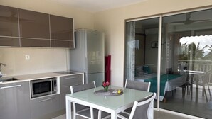 Une cuisine moderne avec un coin repas, un réfrigérateur et une porte-fenêtre coulissante donnant sur un balcon.