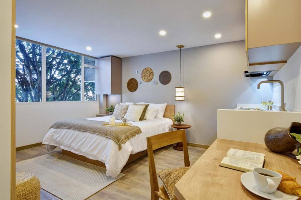 Une chambre moderne avec un grand lit, une table de chevet et une vue sur les arbres par la fenêtre.