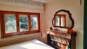 Une chambre avec une grande fenêtre, une commode en bois et un miroir.