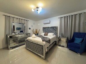 Un dormitorio moderno con una cama grande, un tocador con espejo, un sillón azul y una lámpara en el techo.