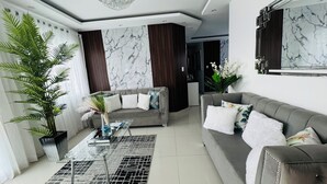 Una sala de estar moderna con un sofá gris, una mesa de centro de cristal y una planta grande en maceta.