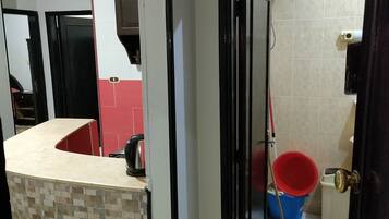 A hallway leading to a bathroom with a checkered floor, a red bucket, and a blue bucket.