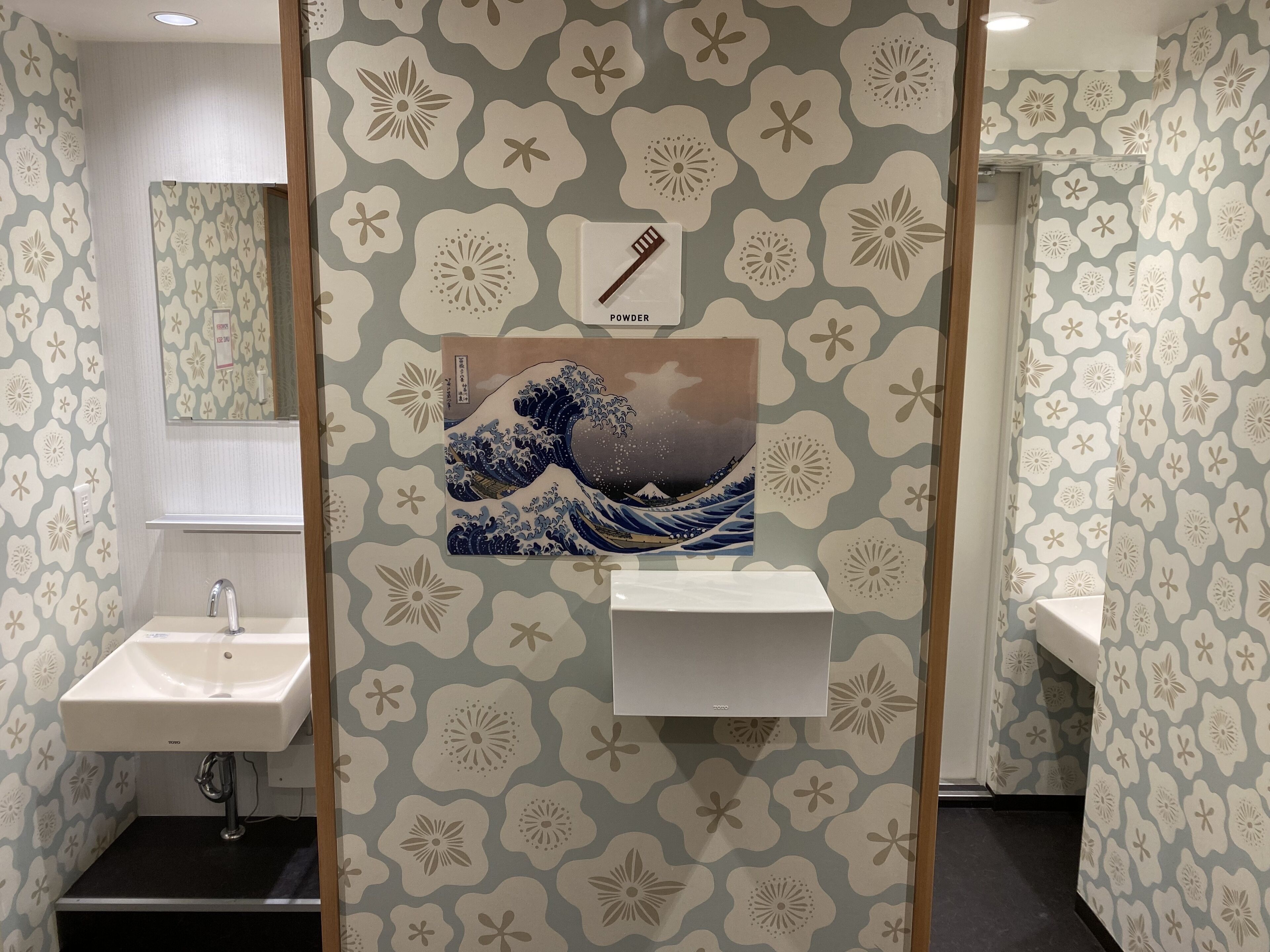 A bathroom with a sink, mirror, and a decorative wall featuring a wave painting.