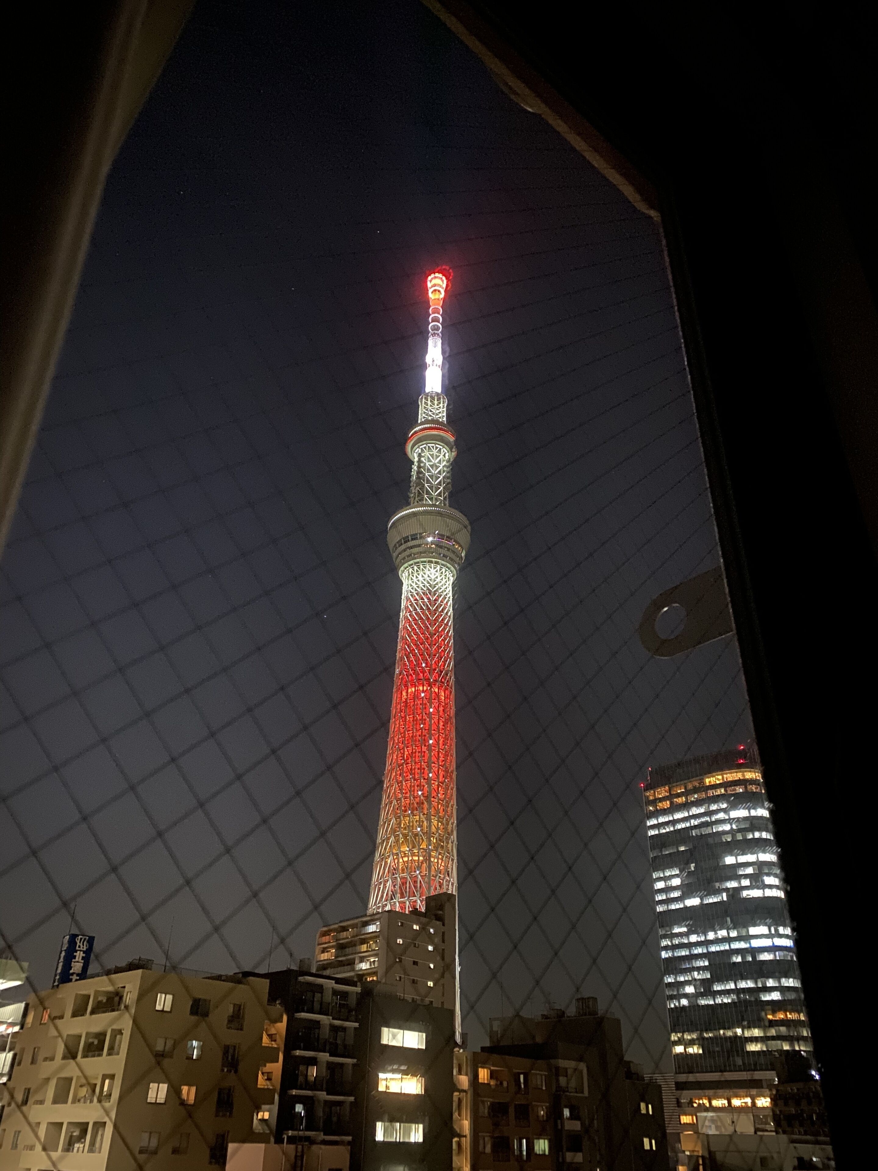 A nighttime view of a tall tower with red and white lights, surrounded by buildings.