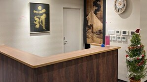 A reception area with a wooden reception desk, a framed artwork, a clock, and a small Christmas tree. - HOTEL WAKO Tokyo Tree View (Tokyo)