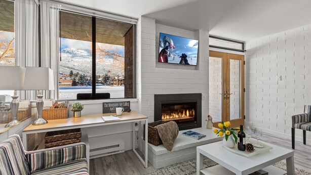 A modern living room with a fireplace, a television mounted above it, and a view of a snowy landscape through large windows. - Great Location for Year-Round Recreation & Luxury Community Amenities + Pet-Friendly! (Park City)