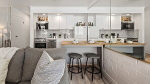 A modern kitchen with white cabinets, a brick backsplash, and a wooden countertop. There is a bar stool and a couch with cushions. - Great Location for Year-Round Recreation & Luxury Community Amenities + Pet-Friendly! (Park City)