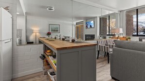 A modern kitchen with a wooden island, a dining area with striped chairs, a grey sofa, and a TV in the background. - Great Location for Year-Round Recreation & Luxury Community Amenities + Pet-Friendly! (Park City)